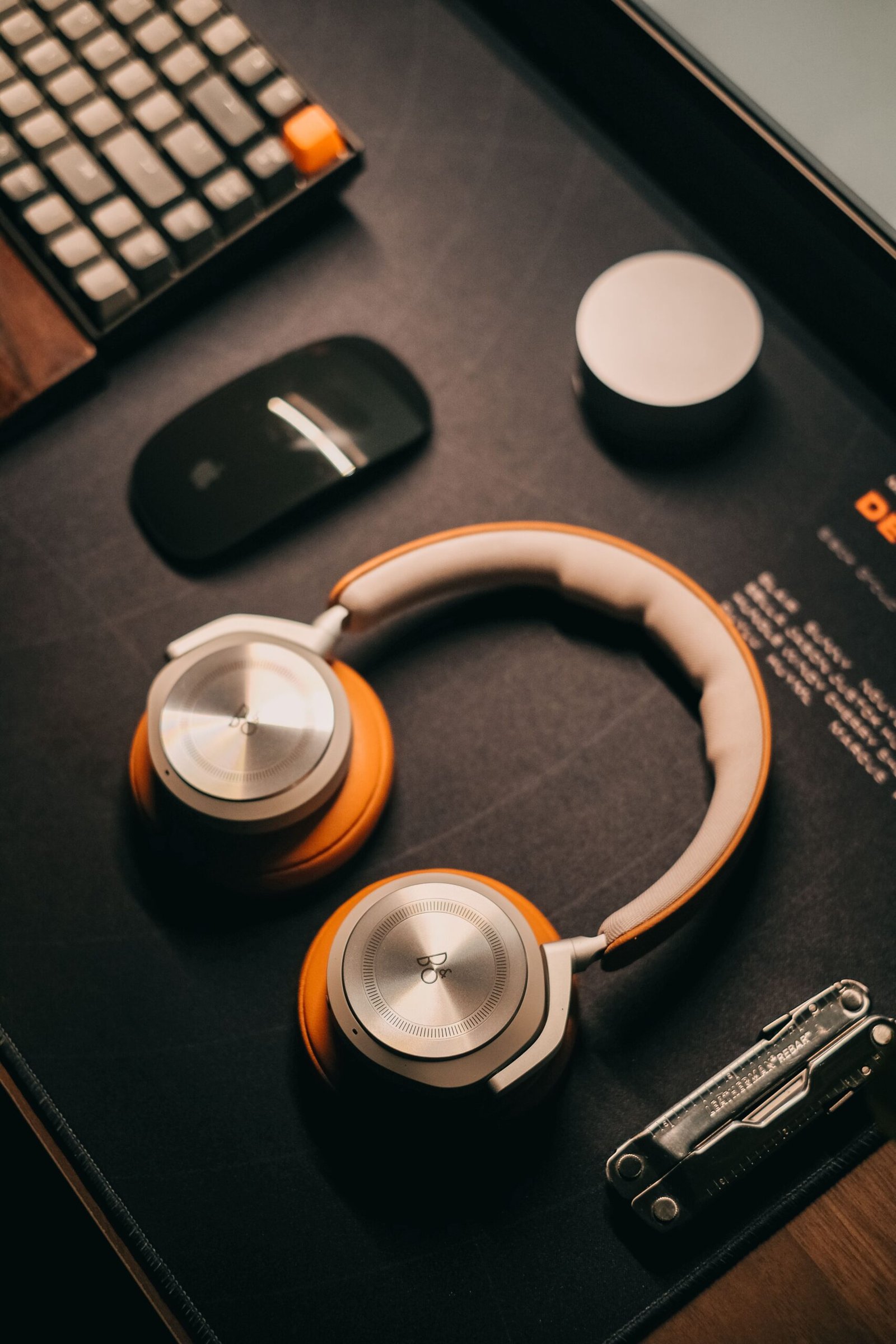 Stylish desk setup featuring orange and silver headphones, a sleek mouse, and keyboard.